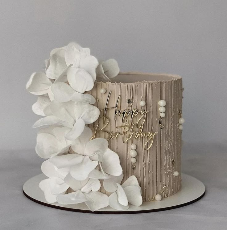 a cake with white flowers on it and the words happy birthday written in gold lettering