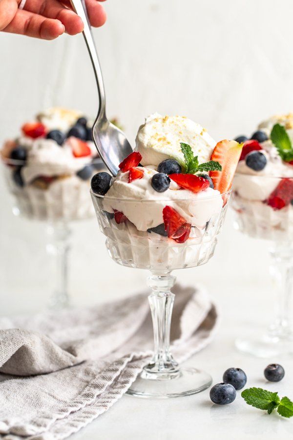 two desserts with berries and whipped cream in small glass dishes on a white table