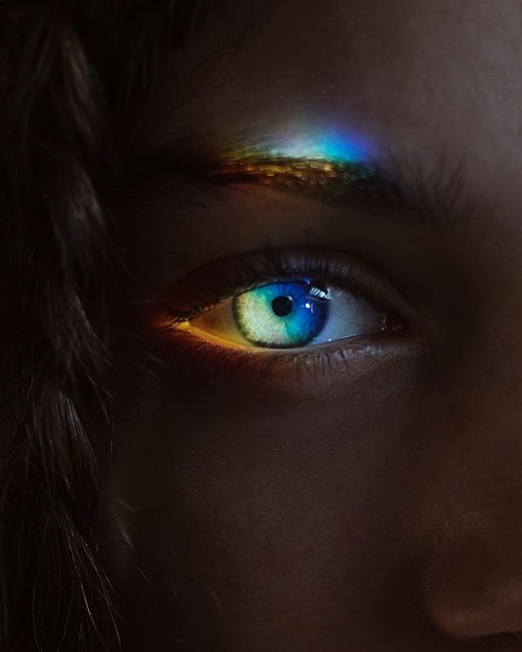 a woman's eyes with bright colored light shining on her face and eyeliner