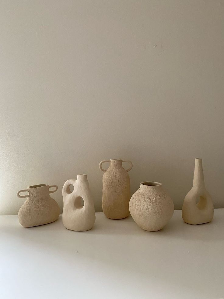 five white vases are lined up in a row on a countertop against a wall