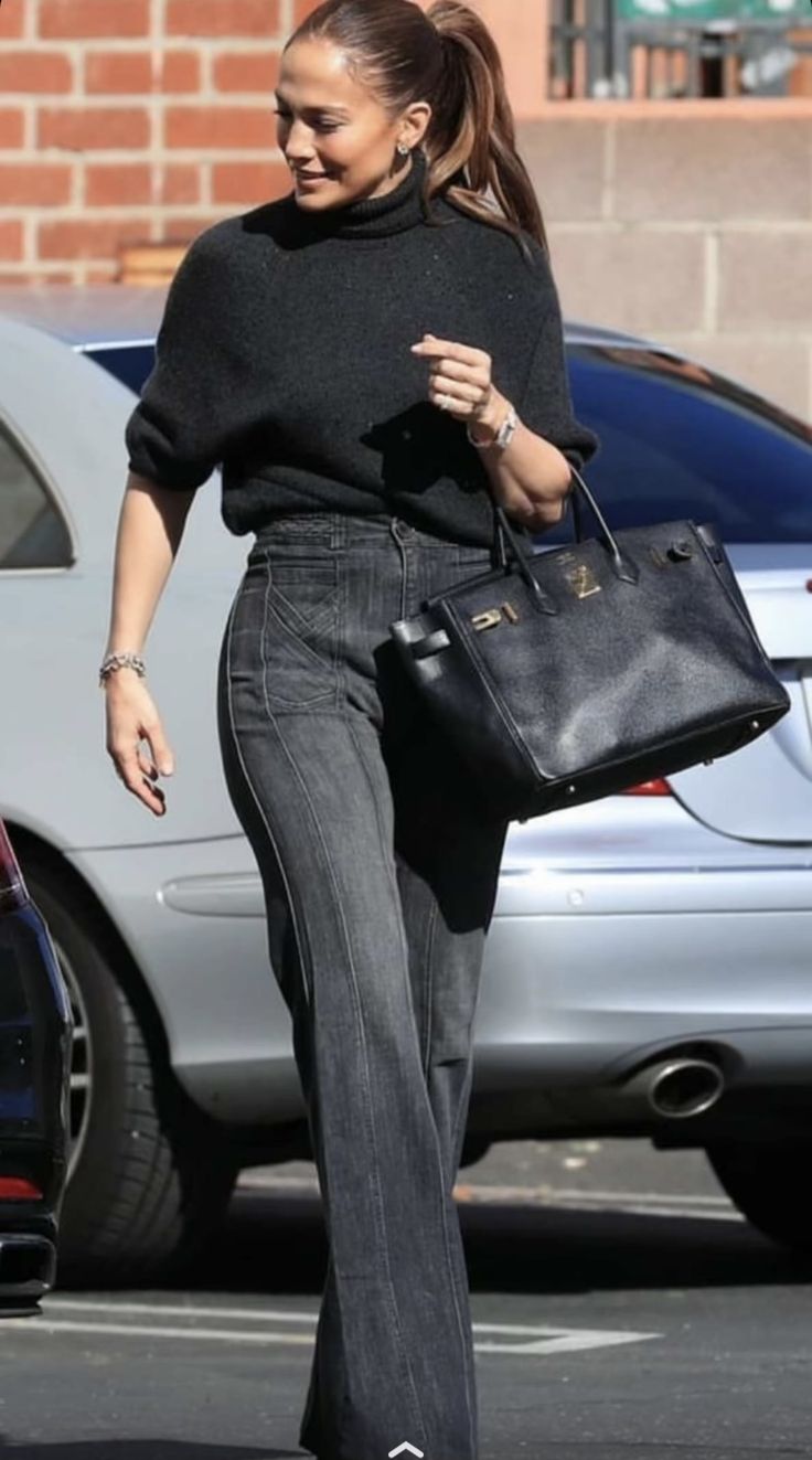 a woman walking down the street carrying a black handbag in her right hand and wearing high heeled shoes