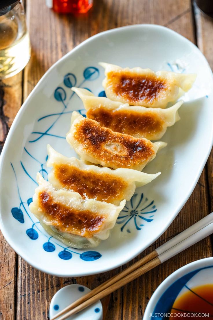 three dumplings on a blue and white plate with chopsticks next to it