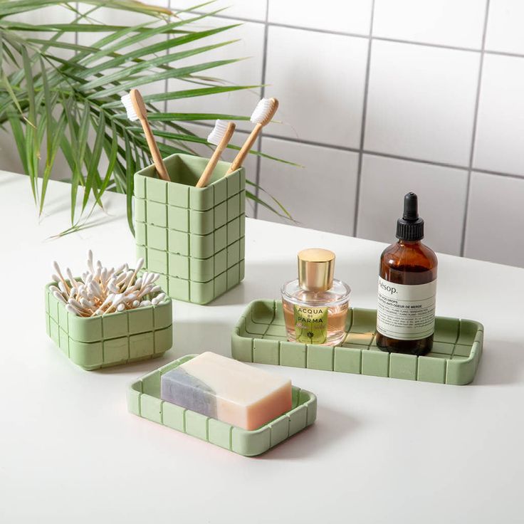 three green containers with soap, toothbrushes and other items on a white counter