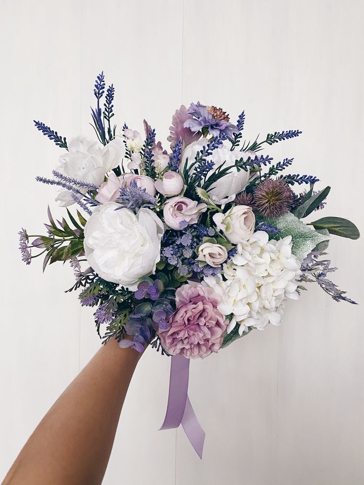 a woman's hand holding a bouquet of white, purple and lilac flowers