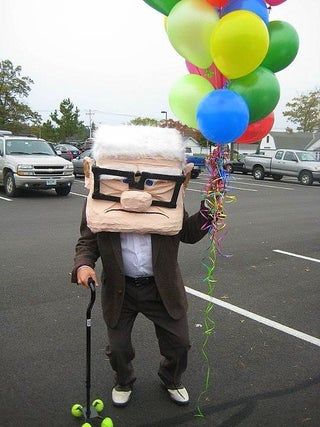 a man in a suit and tie holding up a bunch of balloons with a bag on his head