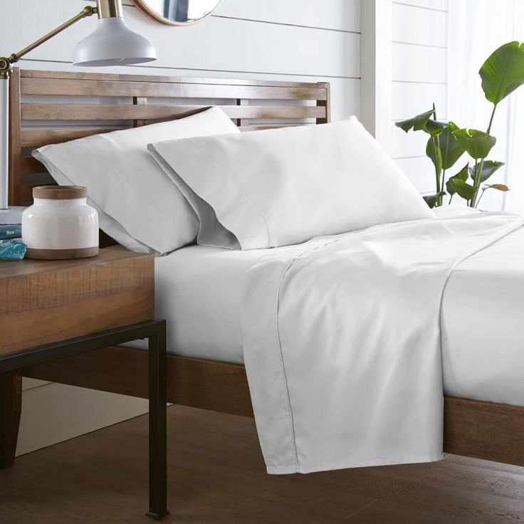 a bed with white sheets and pillows on top of it next to a wooden headboard