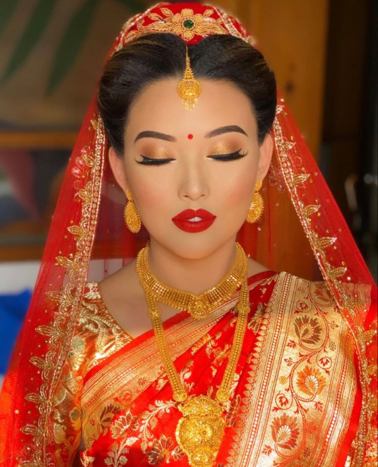 a woman wearing a red and gold bridal outfit with golden jewelry on her head