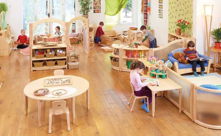 children's playroom with wooden tables and chairs in the center, while adults sit at their desks