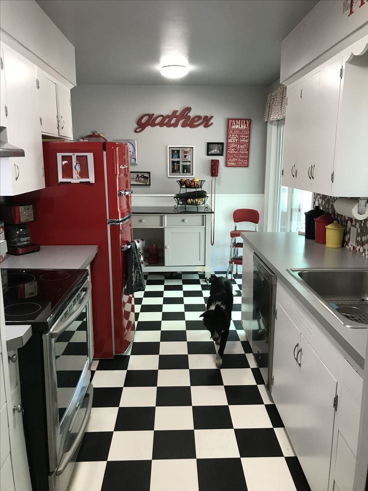 a black and white checkered floor in a kitchen with red refrigerator, stove top oven, and sink