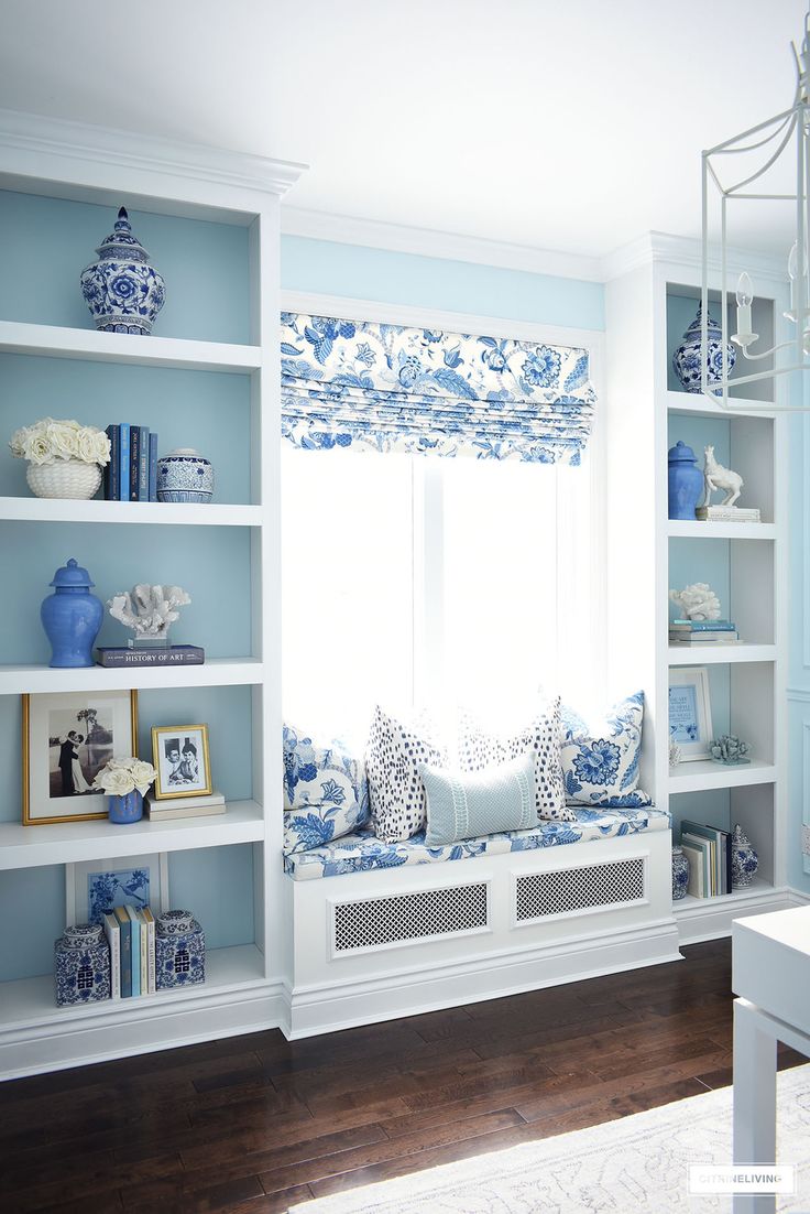 a blue and white living room with bookshelves filled with vases, pillows and pictures