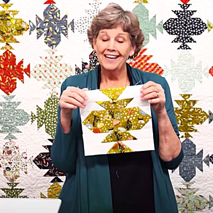 an older woman holding up a piece of paper in front of a quilted wall