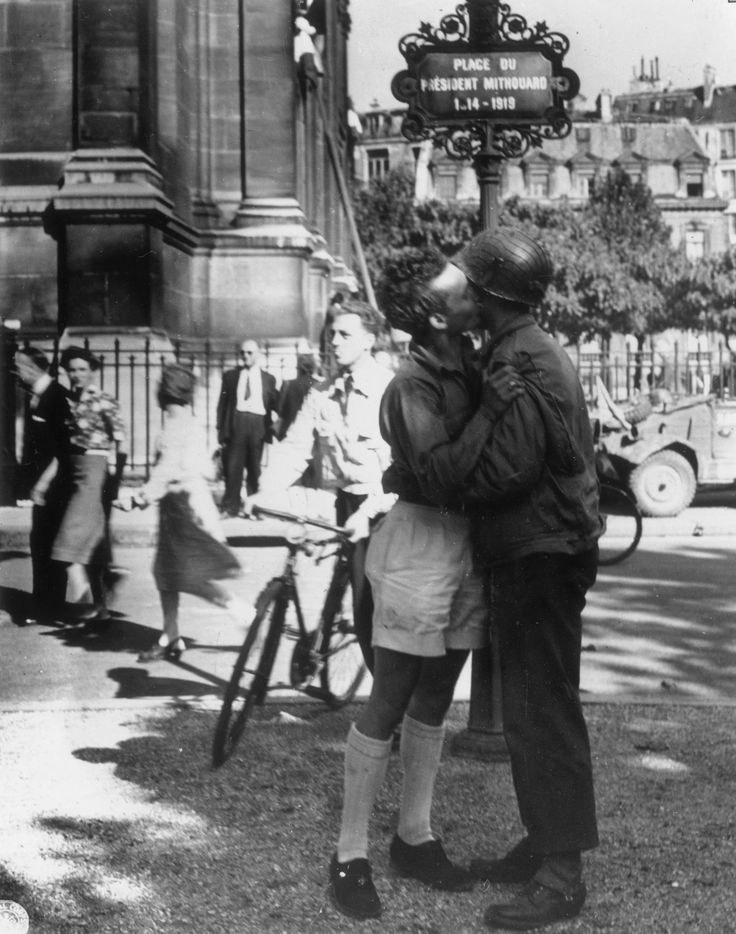 an old black and white photo of two people kissing in front of a street sign