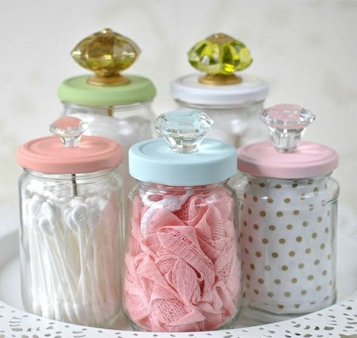 four glass jars with different colored lids on a lace doily and white doily