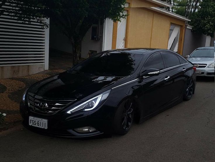 a black car parked in front of a house on the side of a road next to another car