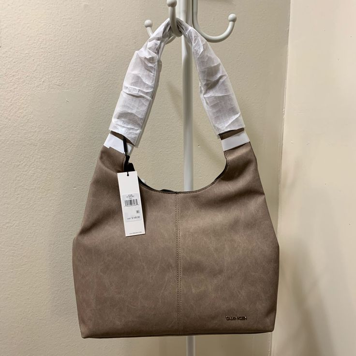 Casual Yet Trendy Hobo Shoulder Bag Perfect Size For Everyday Use Throw All Of Your Essentials Into This Fun Hobo & Get On With Your Day High Quality Vegan Leather 2 Interior Slip Pockets 1 Interior Zip Pocket Removable Pouch Magnetic Closure Approx Dims 13" H X 17" W X 3" D, 13" Handle Drop New W/Tags Better Pricing On Ig Ig: @Ari_sweirdmysteries Modern Calvin Klein Tote Shoulder Bag, Taupe Shoulder Bag With Handles, Calvin Klein Leather Tote Shoulder Bag, Calvin Klein Satchel With Top Carry Handle, Taupe Bags With Handle Drop For Shopping, Modern Calvin Klein Shoulder Bag For Daily Use, Shopping Bag With Handle Drop In Taupe, Calvin Klein Shoulder Satchel, Calvin Klein Tote Bag With Top Carry Handle