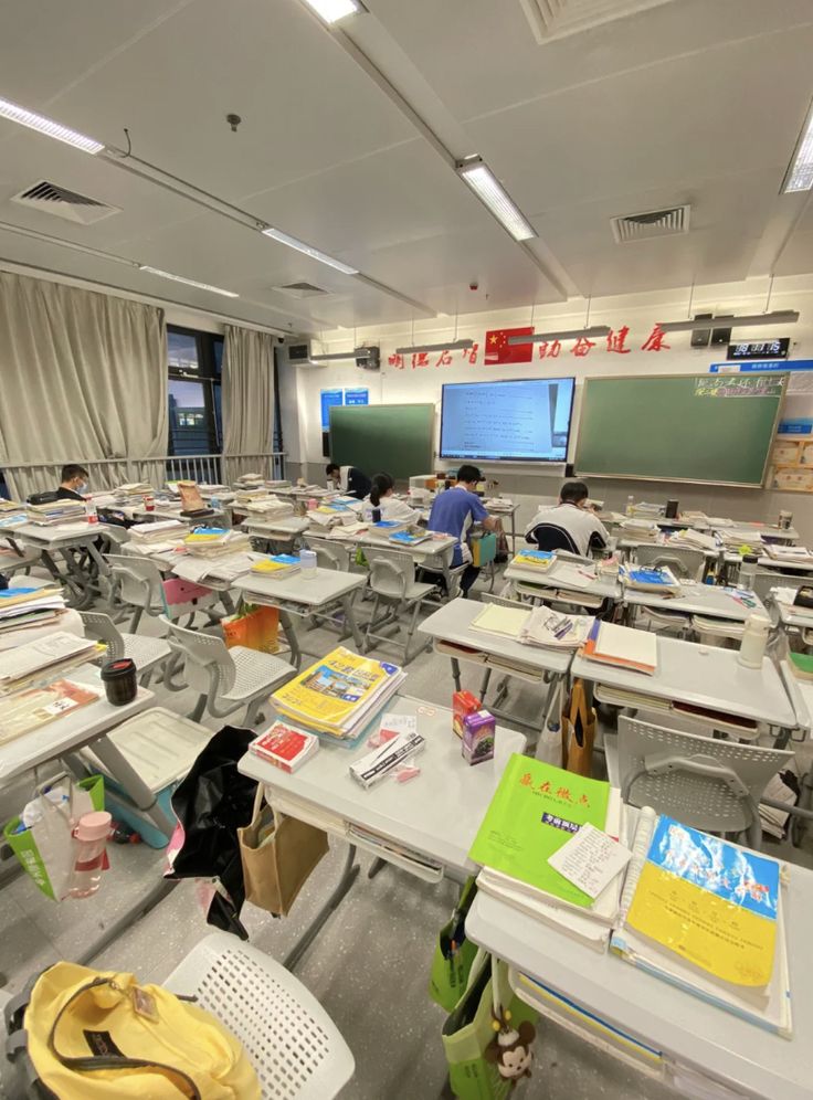 there are many desks in the classroom with books on them and people sitting at their desks