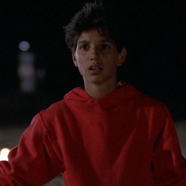 a young man wearing a red hoodie standing in the dark