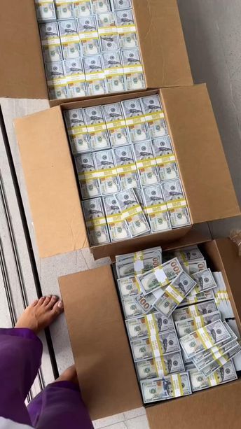 stacks of money are stacked on top of each other in cardboard boxes, with one woman's hand reaching for the stack