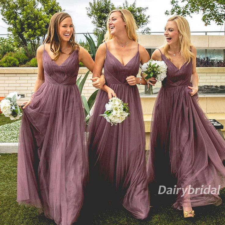 three bridesmaids in long purple dresses laughing at each other on the grass outside