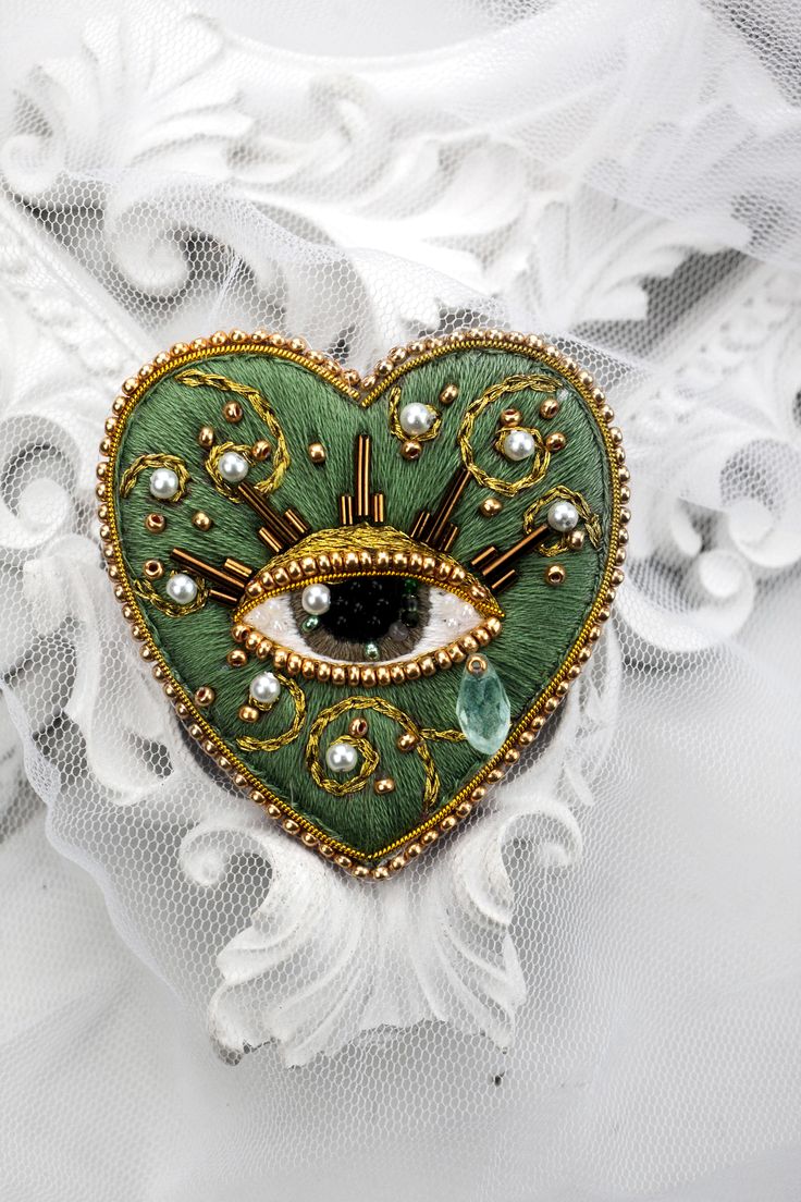 a green heart shaped brooch with an eye on it's center surrounded by pearls