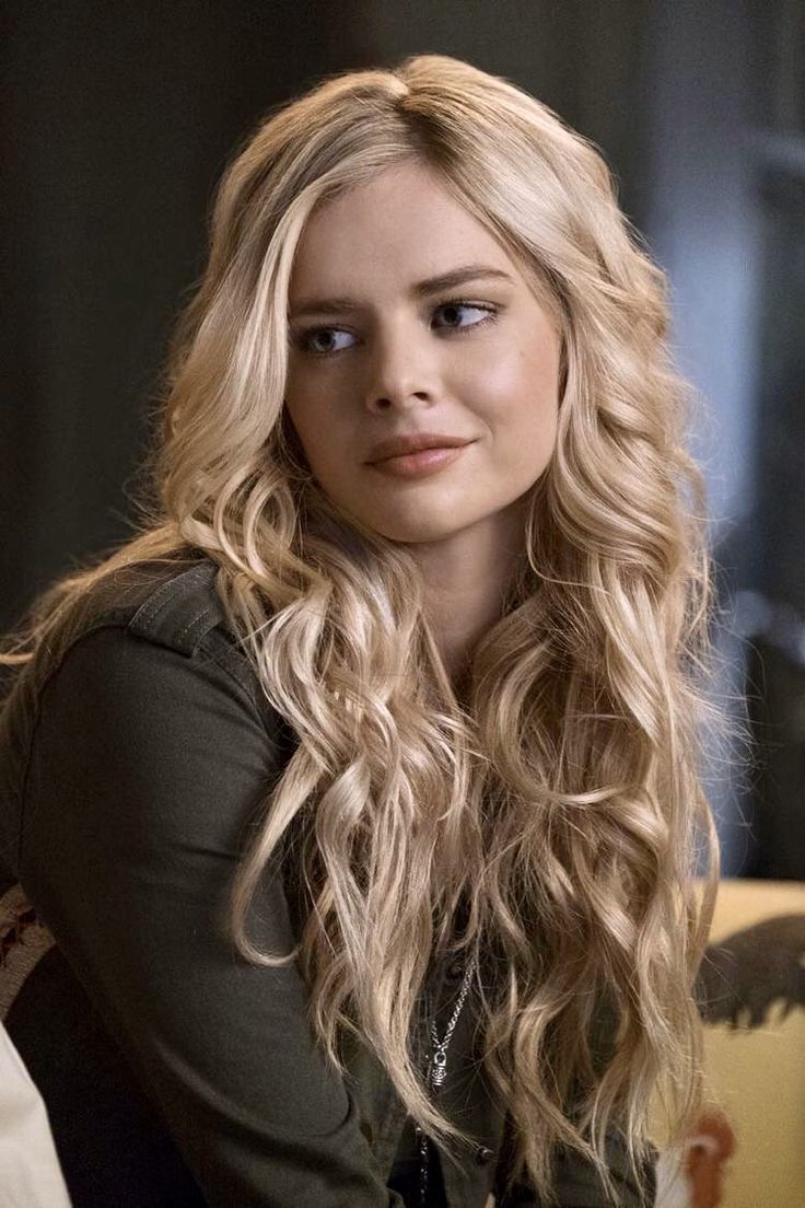 a woman with long blonde hair sitting in front of a chair and looking at the camera