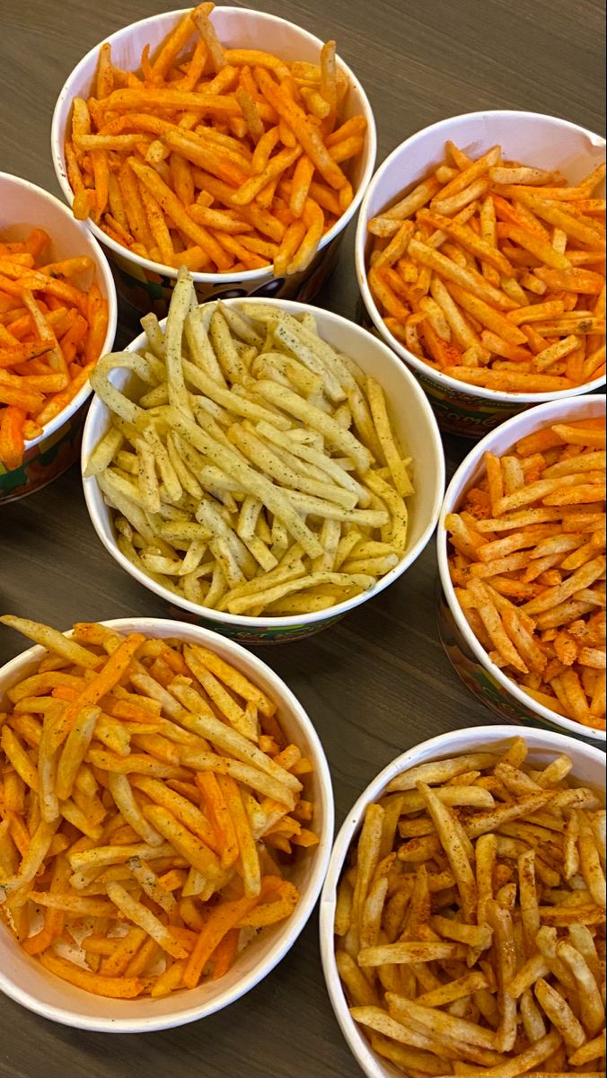 several bowls filled with different types of french fries on a wooden table next to each other