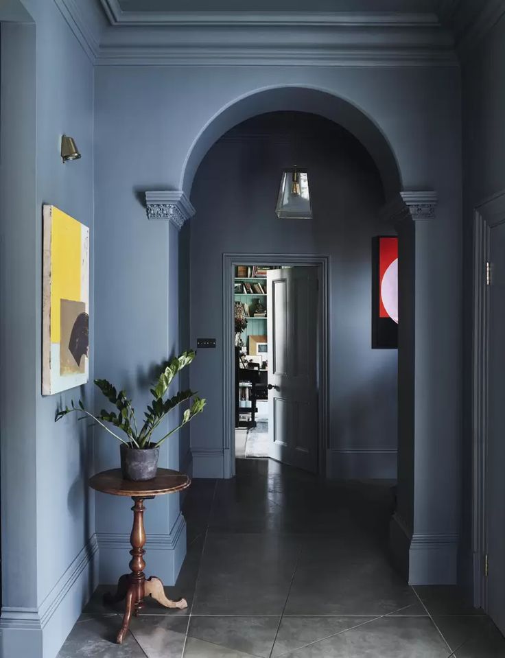 a hallway with blue walls and an arch leading to the dining room, which has a potted plant on a small table