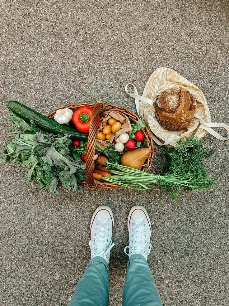 a person standing next to a basket full of vegetables on the ground with their feet propped up