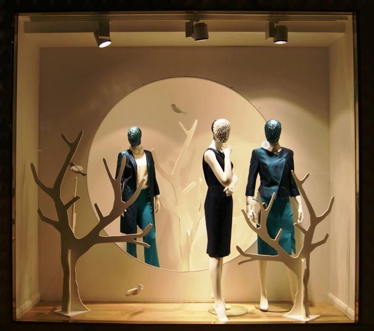 three mannequins dressed in black and blue outfits with trees on the wall