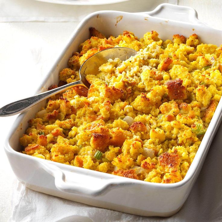 a white casserole dish filled with stuffing and topped with a serving spatula