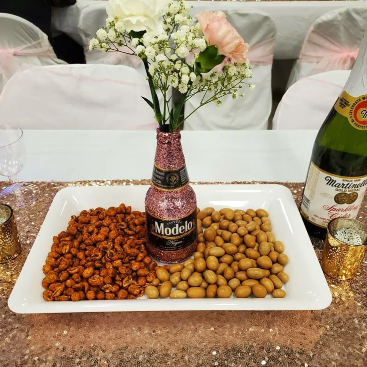 a tray with nuts, champagne and flowers on it next to two bottles of wine