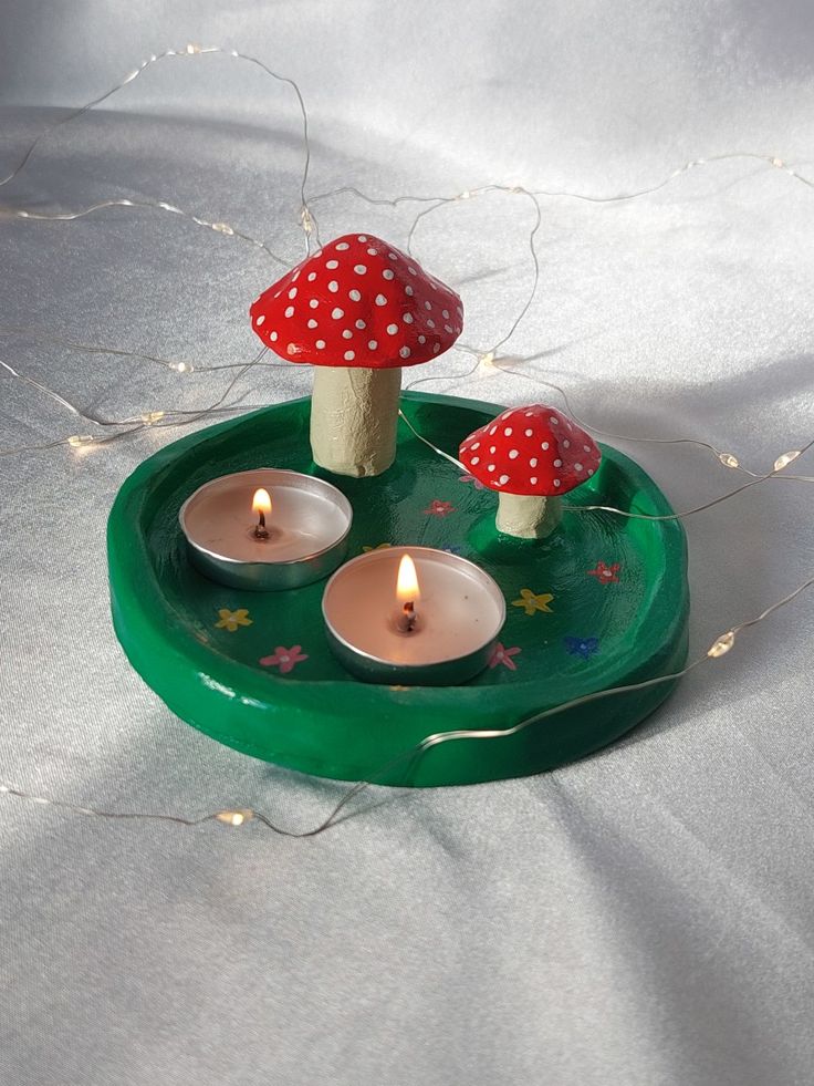 three lit candles are placed on a green tray with mushrooms and stars around it,