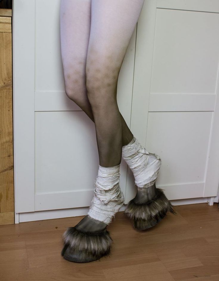 the legs and ankles of a woman in white stockings with furry shoes, standing against a wall