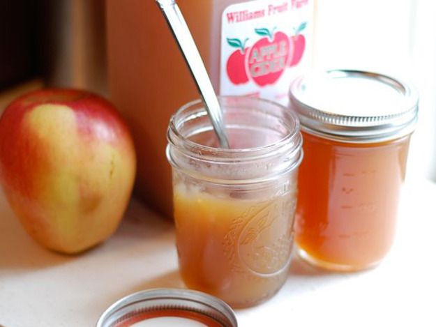 two jars filled with liquid next to an apple and a spoon on top of a table