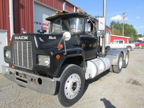 a large black truck parked in front of a red building with other trucks behind it