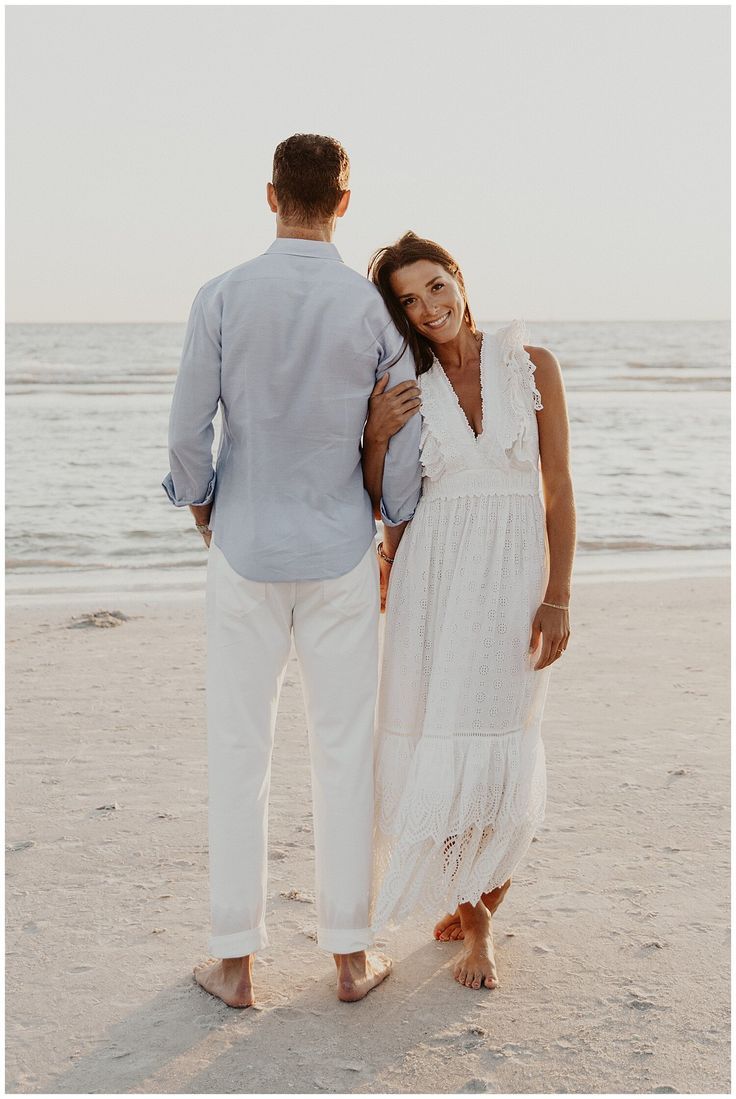 a man and woman are walking on the beach holding each other's hands as they look into the distance