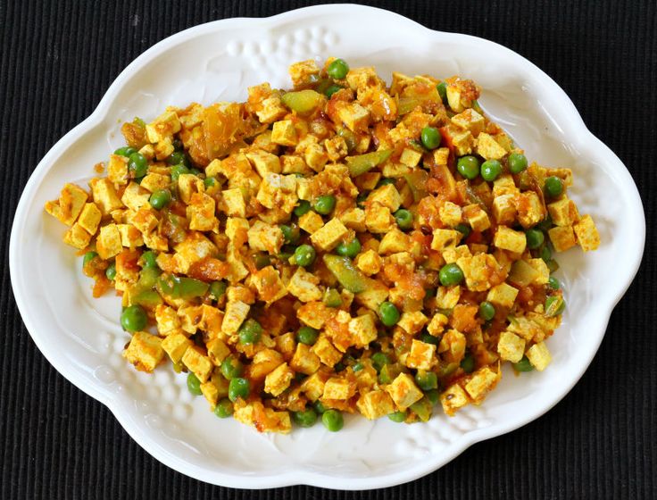 a white plate filled with tofu and peas on top of a black tablecloth