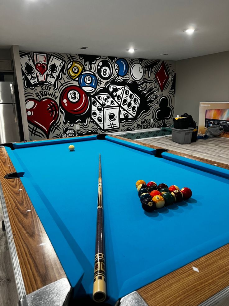 a pool table with cues and balls in front of a wall mural on the wall