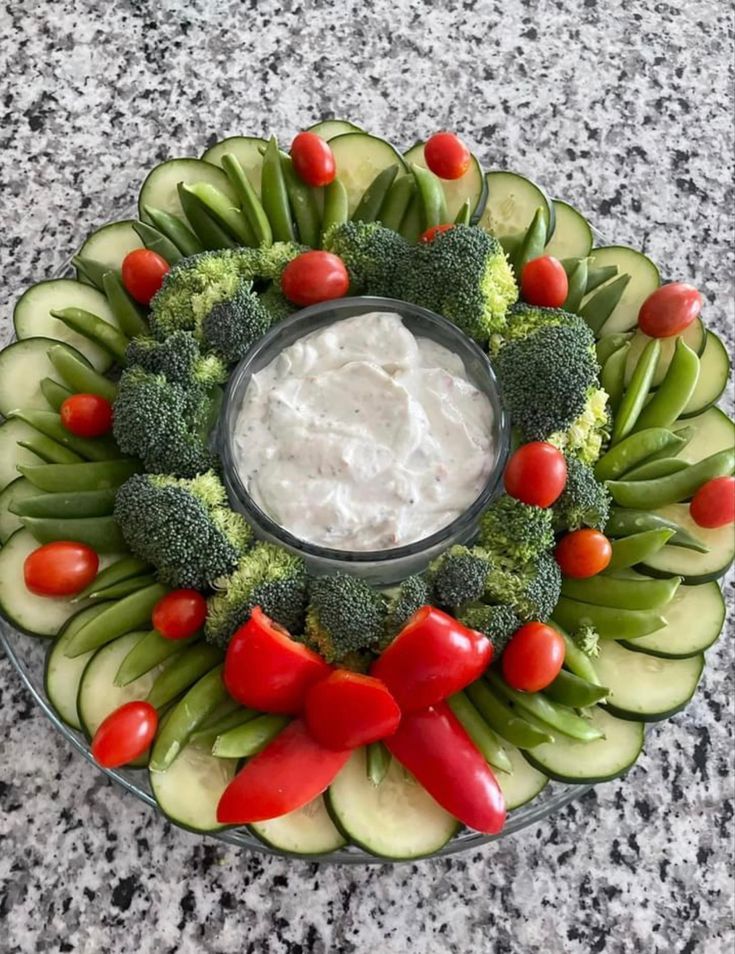 a platter filled with cucumbers, tomatoes, broccoli and dip