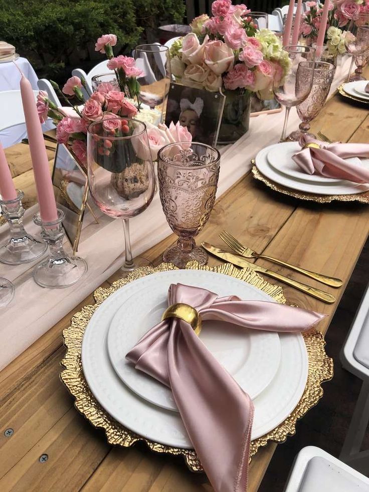 the table is set with pink flowers and gold place settings for an elegant dinner party