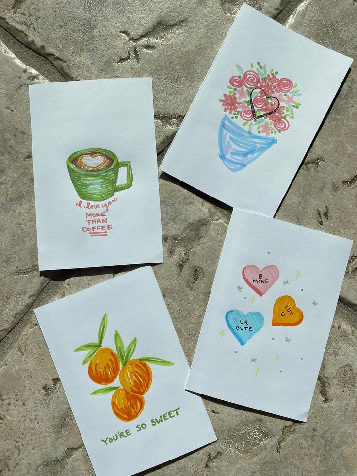 four handmade greeting cards with flowers and hearts on them, sitting on a stone surface