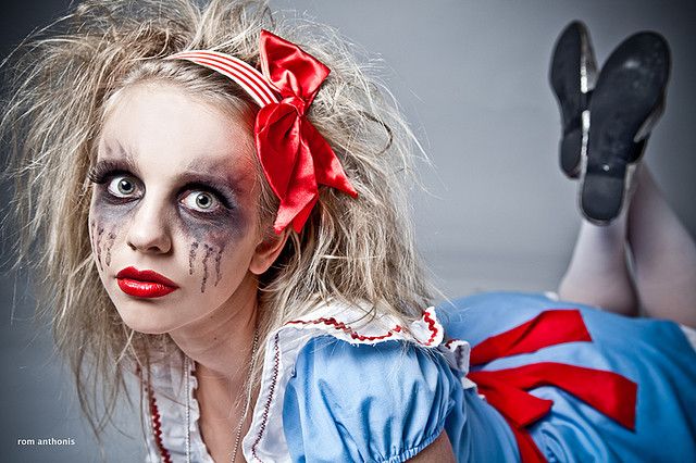 a woman dressed as a clown laying on the ground with her legs crossed and face painted red