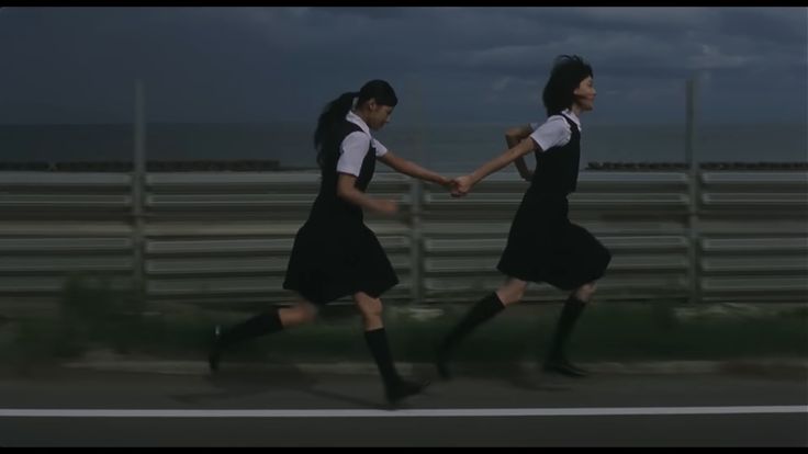 two girls in school uniforms holding hands while walking down the street with dark clouds overhead