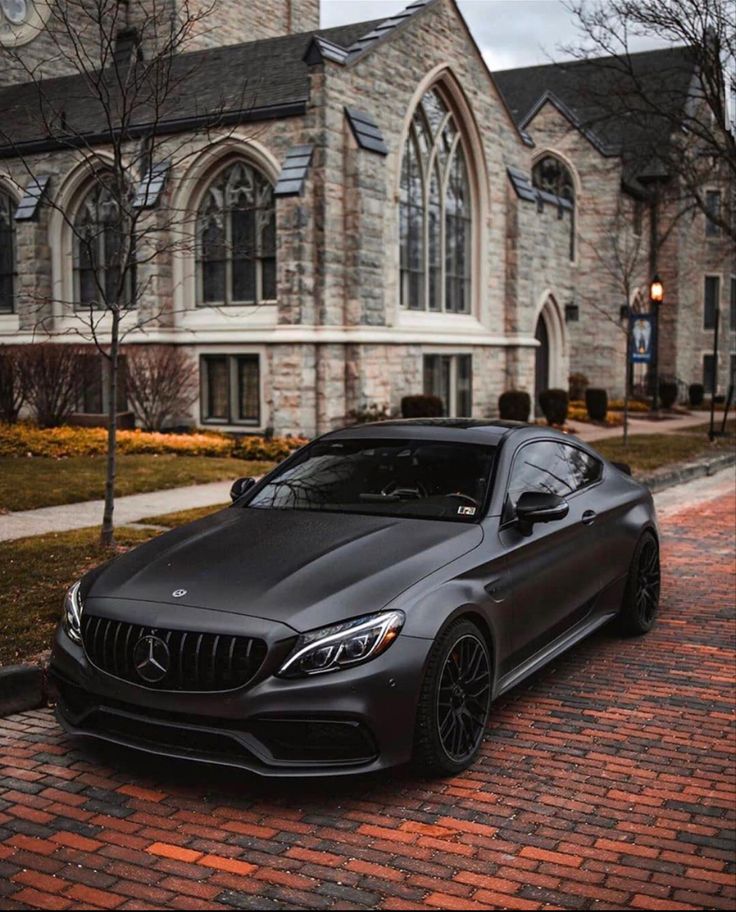 a black car parked in front of a large building on a brick road next to trees