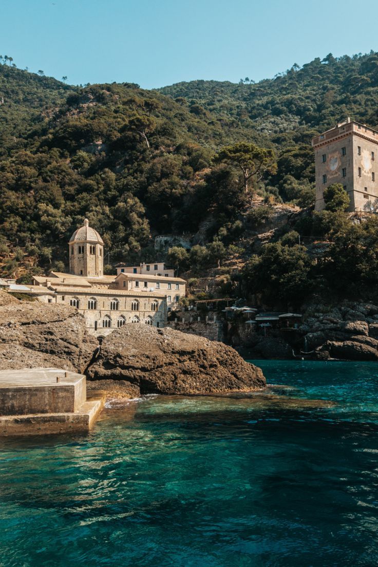 an old building sitting on top of a cliff next to the ocean with clear blue water