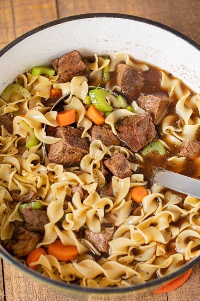 a pot filled with beef noodle soup on top of a wooden table