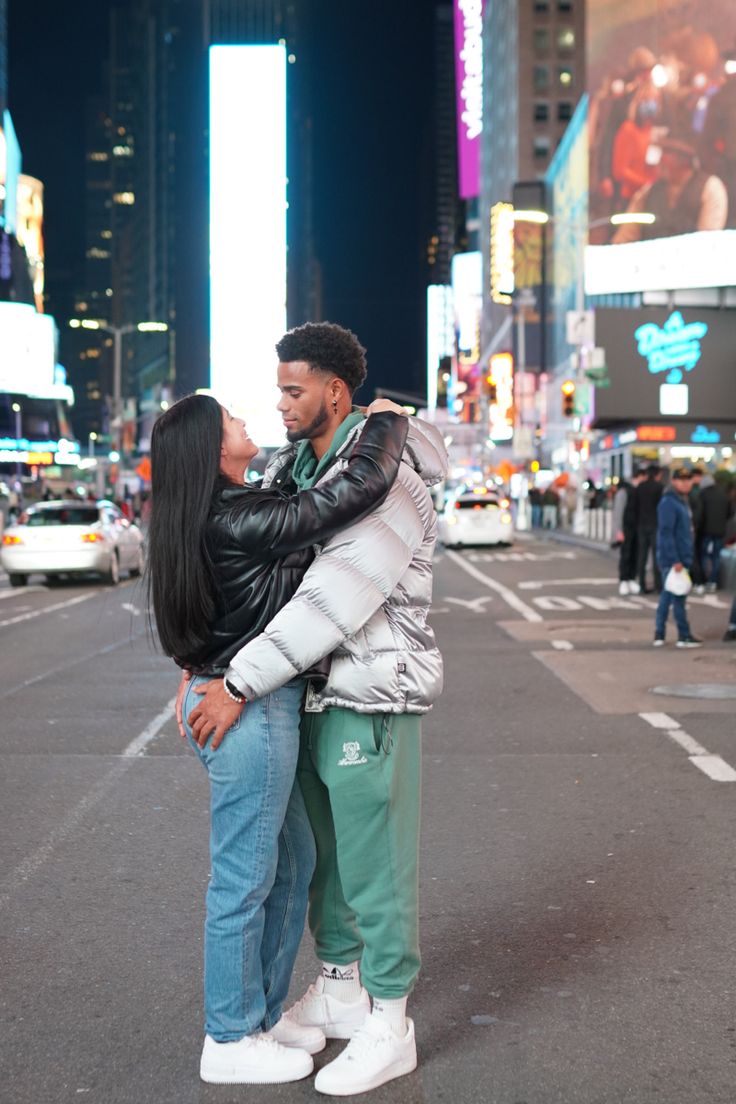 a man and woman standing in the middle of a city street at night, kissing