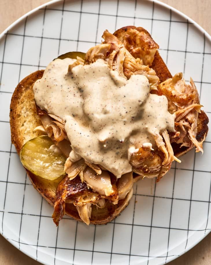 a white plate topped with an open face sandwich covered in gravy and pickles