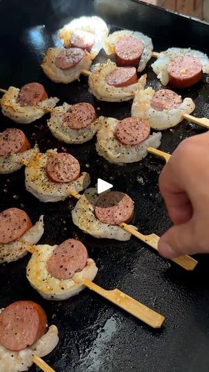 someone is cooking some meat on skewers with wooden sticks in front of them