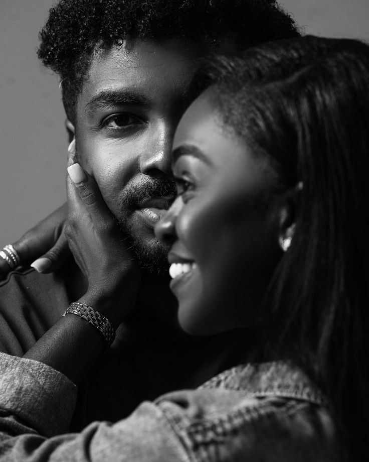 a black and white photo of a couple smiling at each other with their hands on their face